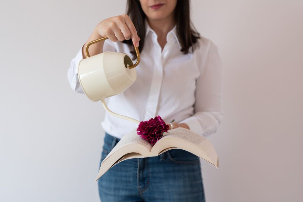 donna freelance con camicia bianca che annaffia un fiore sopra un libro