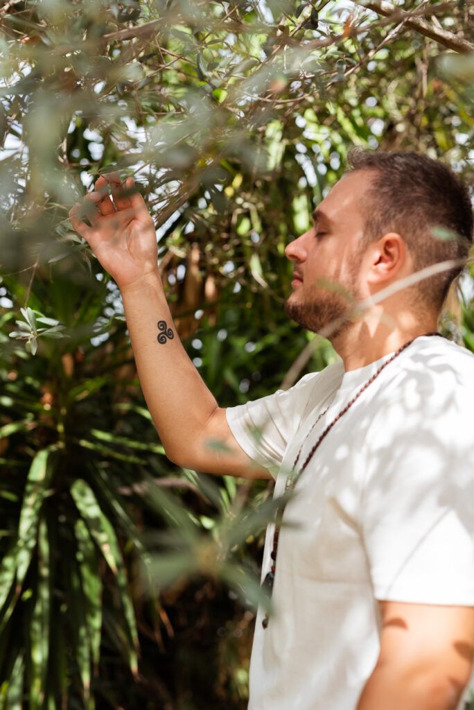 ritratto naturopata immerso nella natura con mano che tocca albero e dettaglio di tatuaggio