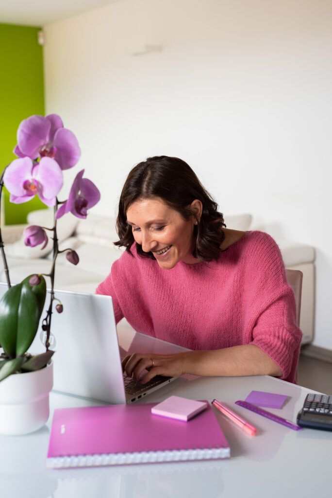 ritratto femminile personal brand con donna sorridente e maglia fuxsia mentre scrive a computer
